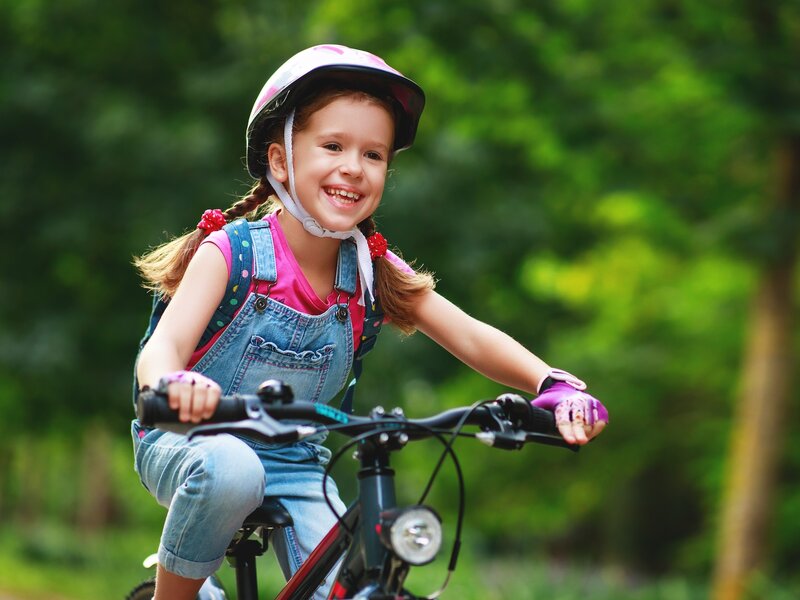 Ein Mädchen mit Fahrradhelm fährt auf einem Fahrrad durch eine grüne Umgebung.