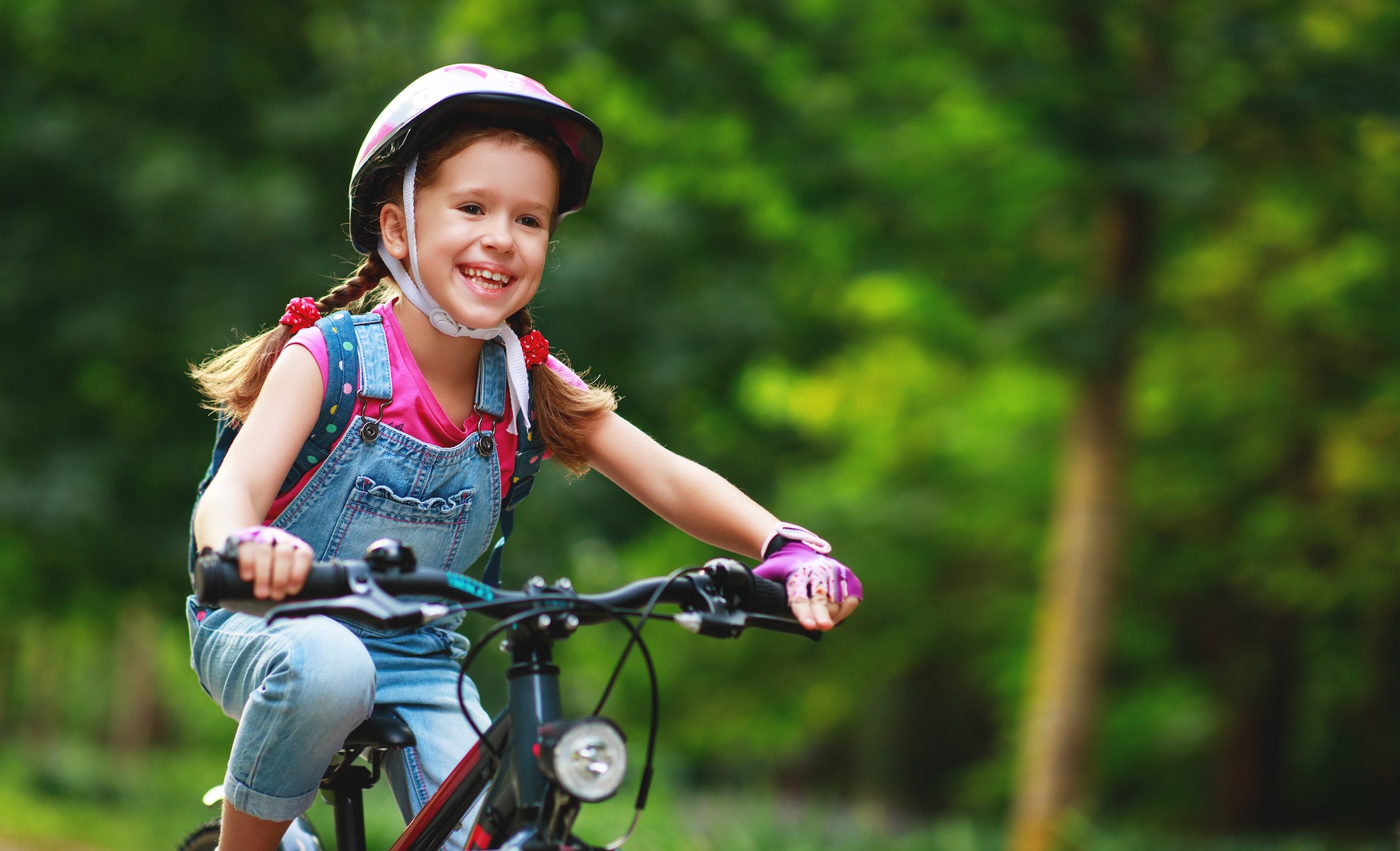 Ein Mädchen mit Fahrradhelm fährt auf einem Fahrrad durch eine grüne Umgebung.
