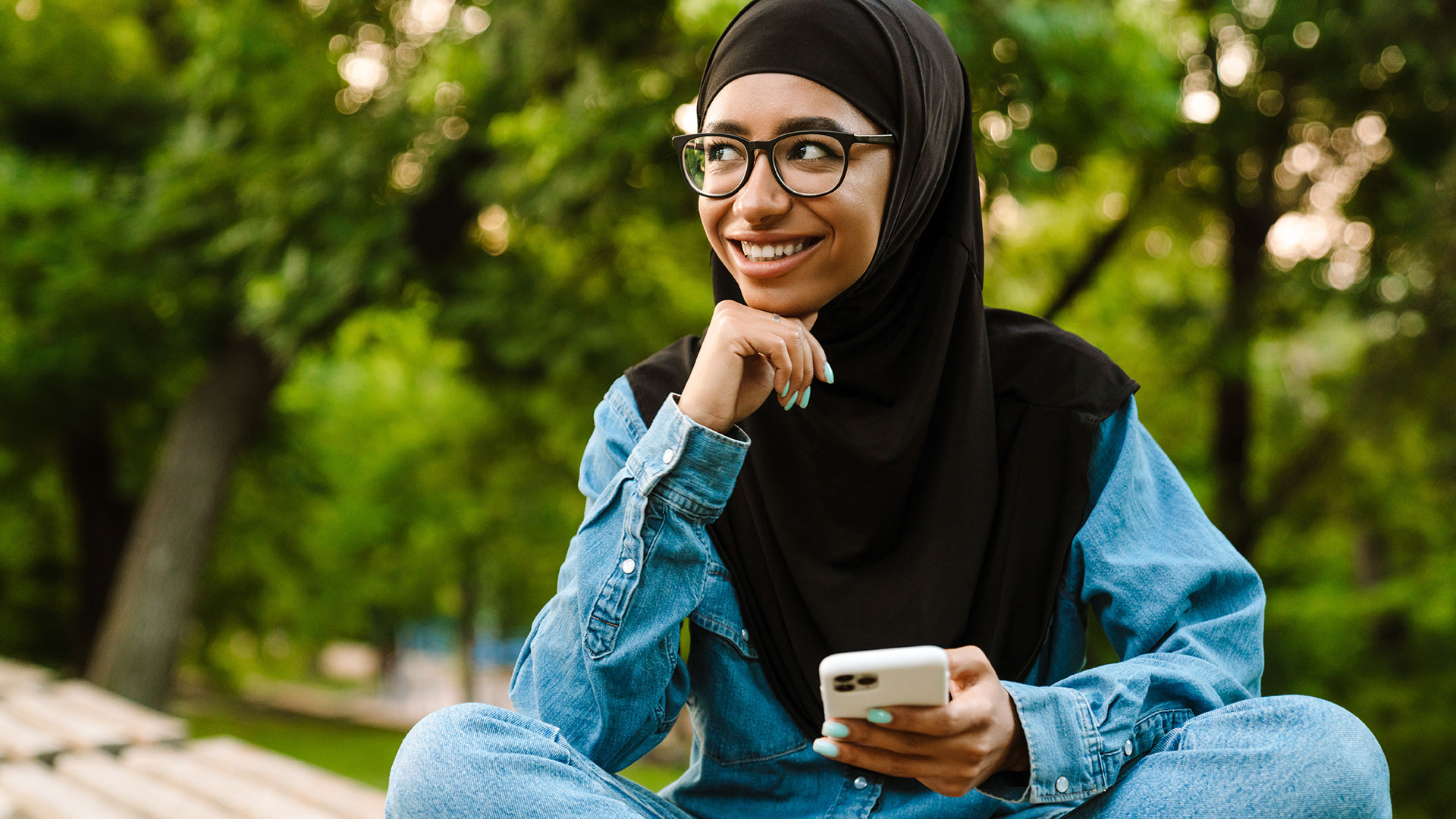 Mädchen im Schneidersitz lächelt, hält Mobiltelefon in der Hand