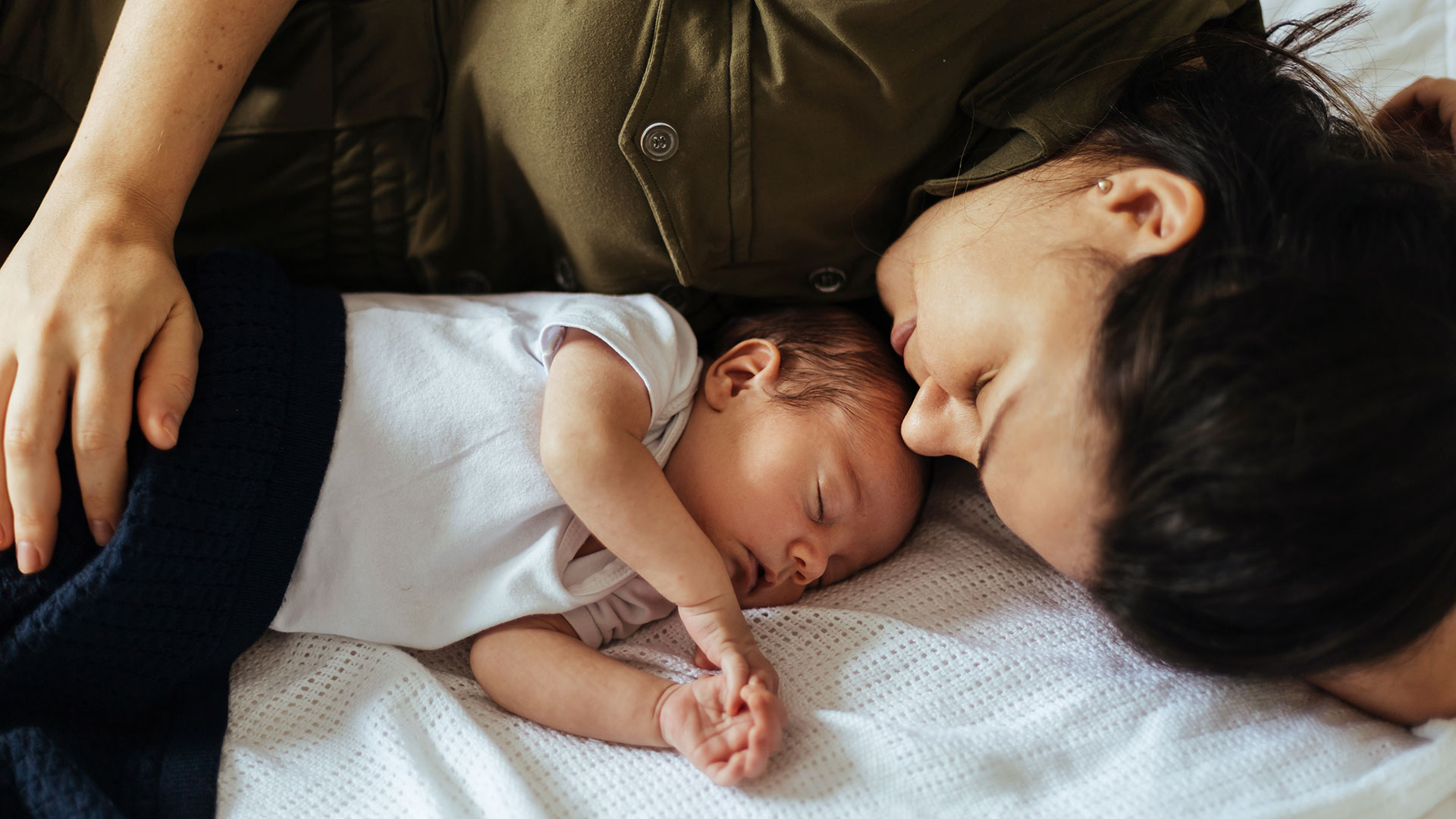 Eine Frau liegt mit einem Säugling schlafend auf dem Bett