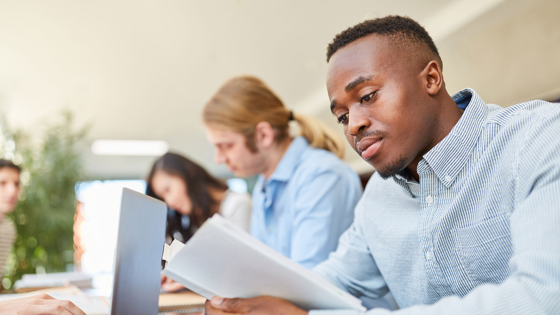 Lernende sitzen an einem Tisch, junger Mann vorne schaut in Unterlagen