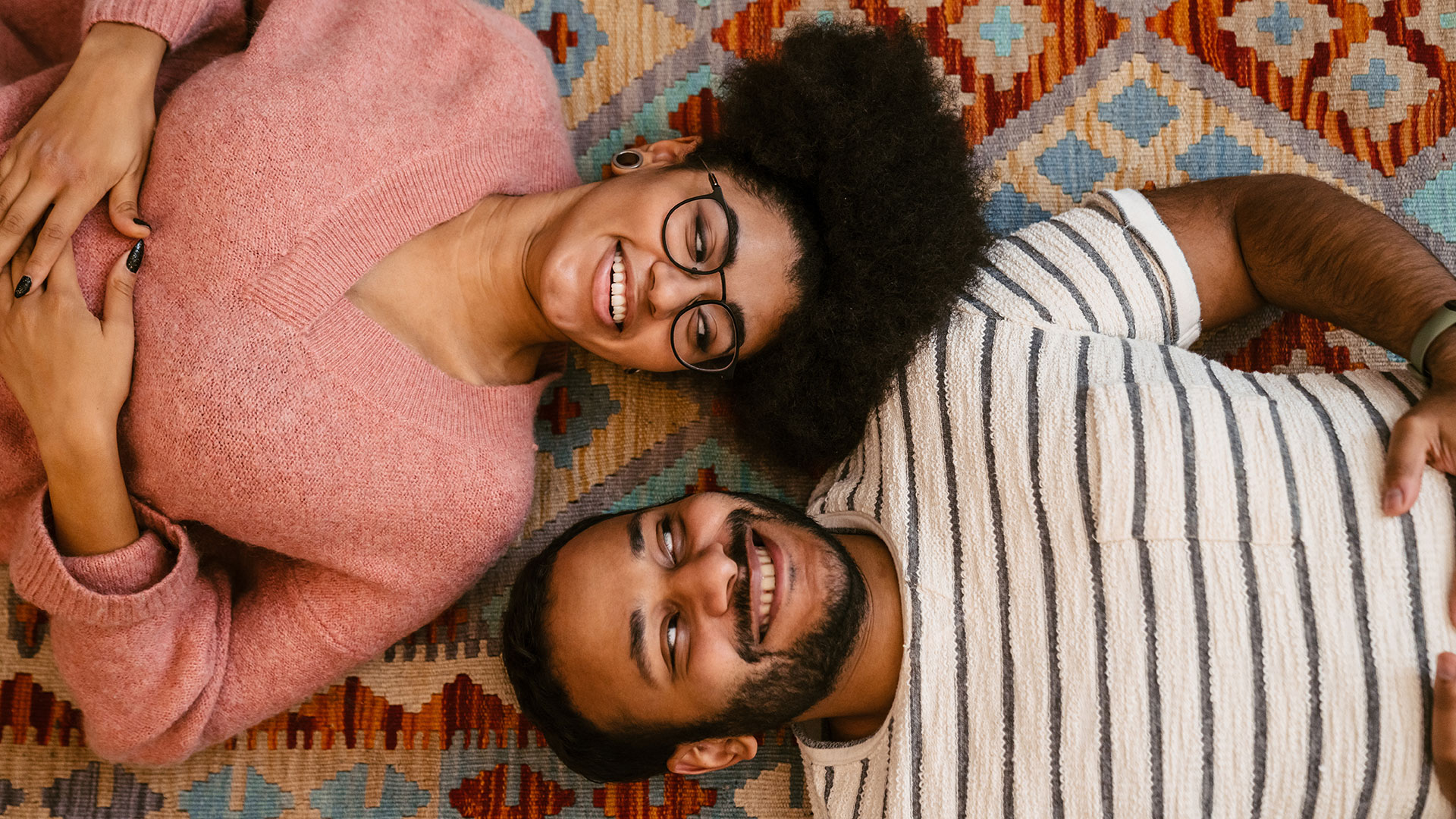 Mann und Frau liegen auf einem Teppich, schauen sich grinsend an