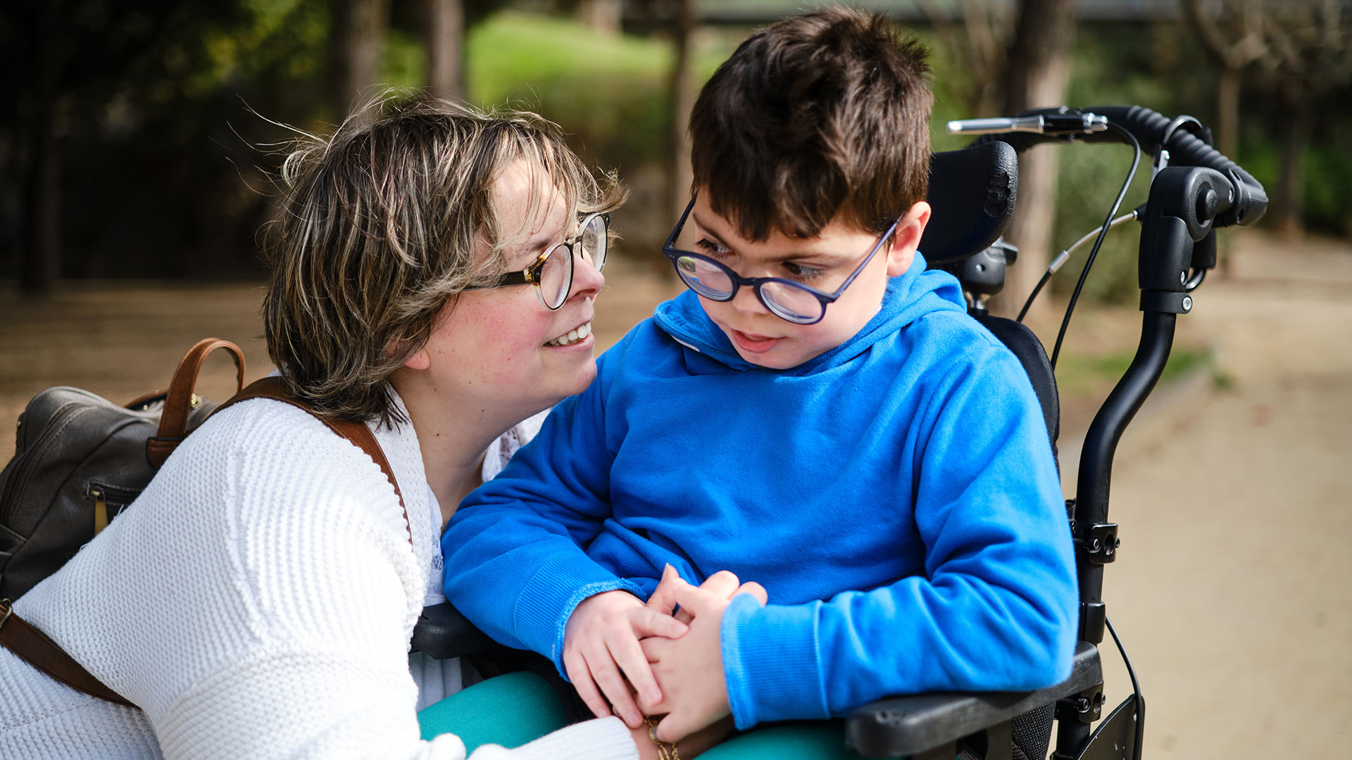 Frau kniet sich nach unten zu einem Kind im Rollstuhl