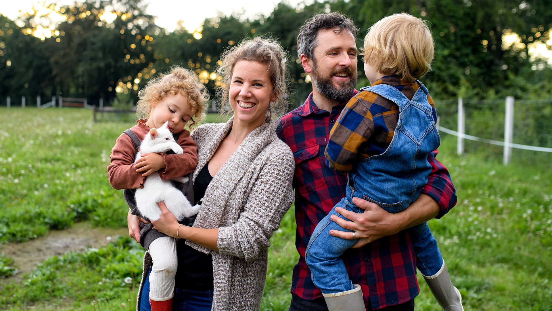 Ein Vater und eine Mutter stehen auf einer Wiese und halten ihre Kinder auf den Armen