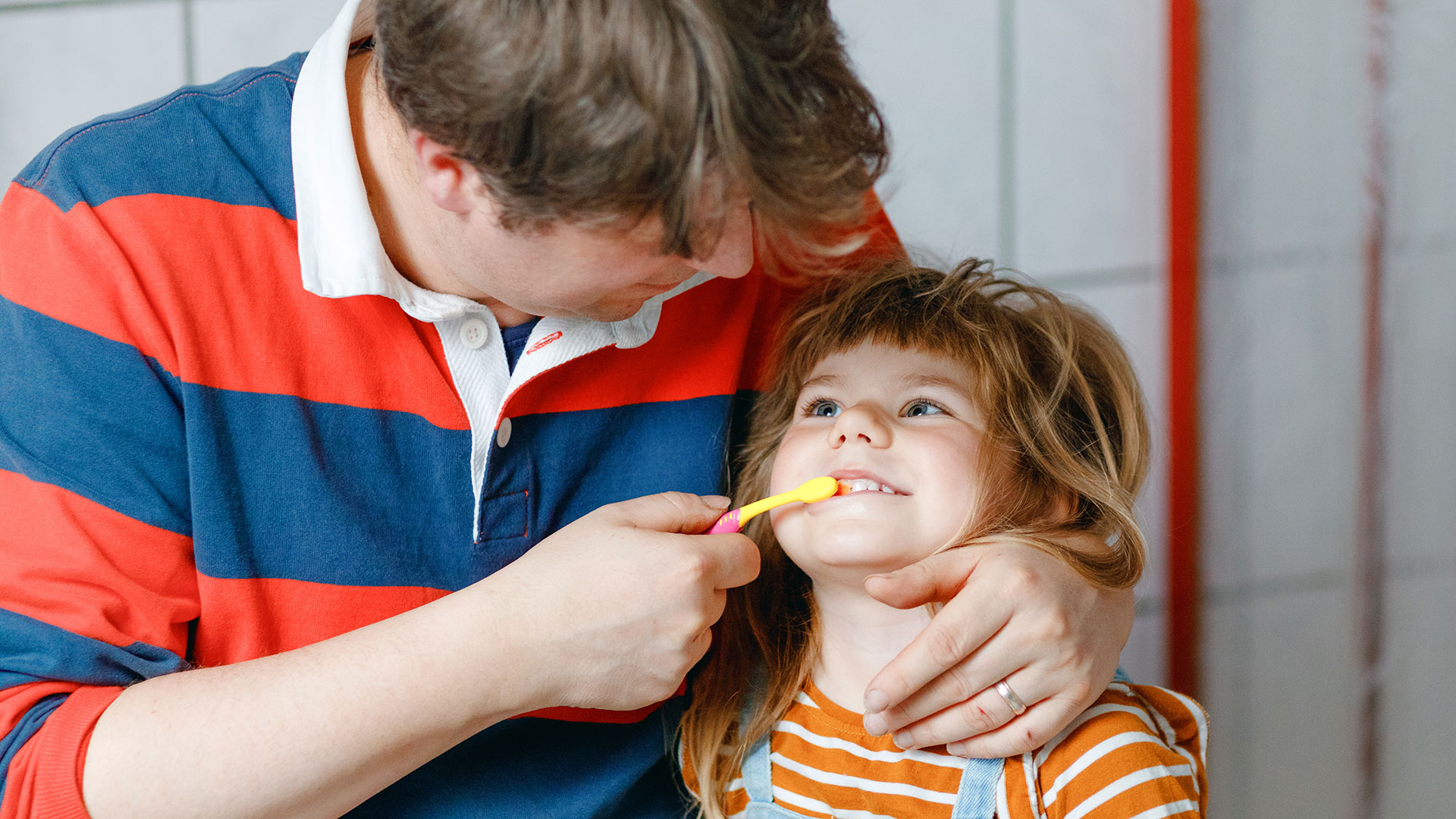 Ein Vater putzt seiner kleinen Tochter die Zähne.