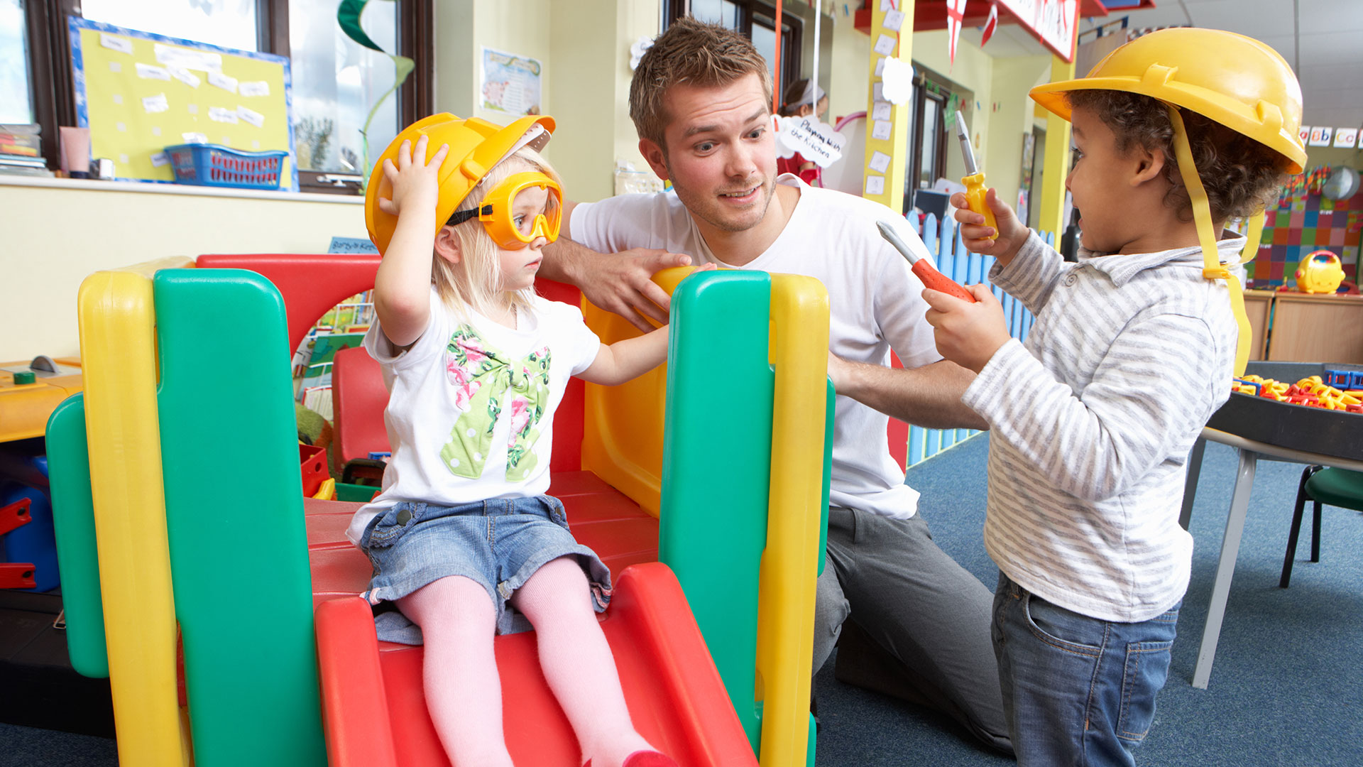 Ein Mann spielt mit zwei Kindern in einer Kita.