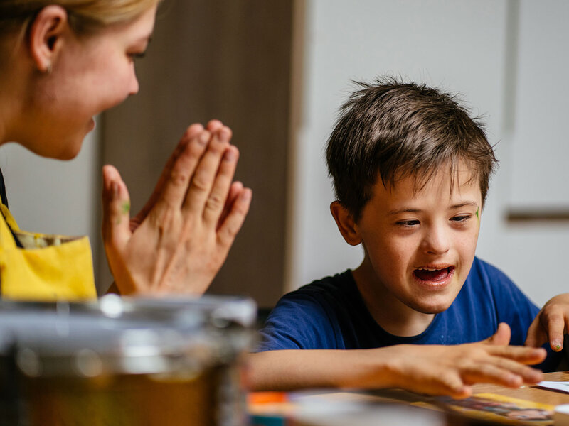Lehrerin klatscht in die Hände, um ein Kind mit Behinderung zu motivieren