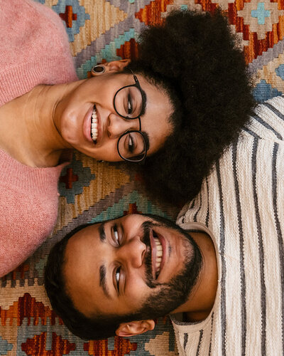 Mann und Frau liegen auf einem Teppich, schauen sich grinsend an