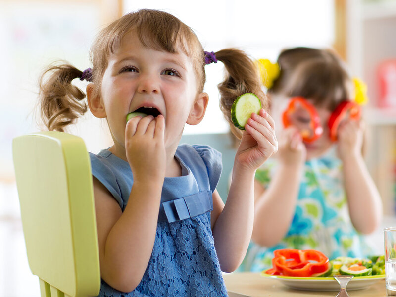 Zwei Mädchen essen rohes Gemüse im Kindergarten.