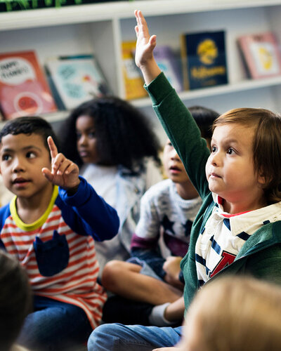 Kinder sitzen auf dem Boden, ein Kind in der Mitte zeigt auf
