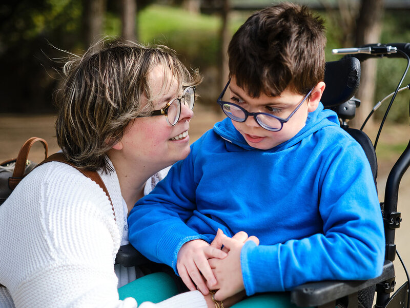 Frau kniet sich nach unten zu einem Kind im Rollstuhl