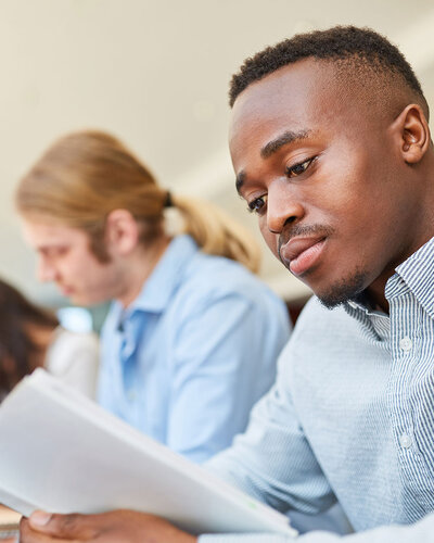 Lernende sitzen an einem Tisch, junger Mann vorne schaut in Unterlagen