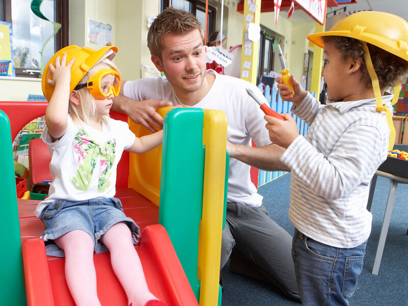 Ein Mann spielt mit zwei Kindern in einer Kita.