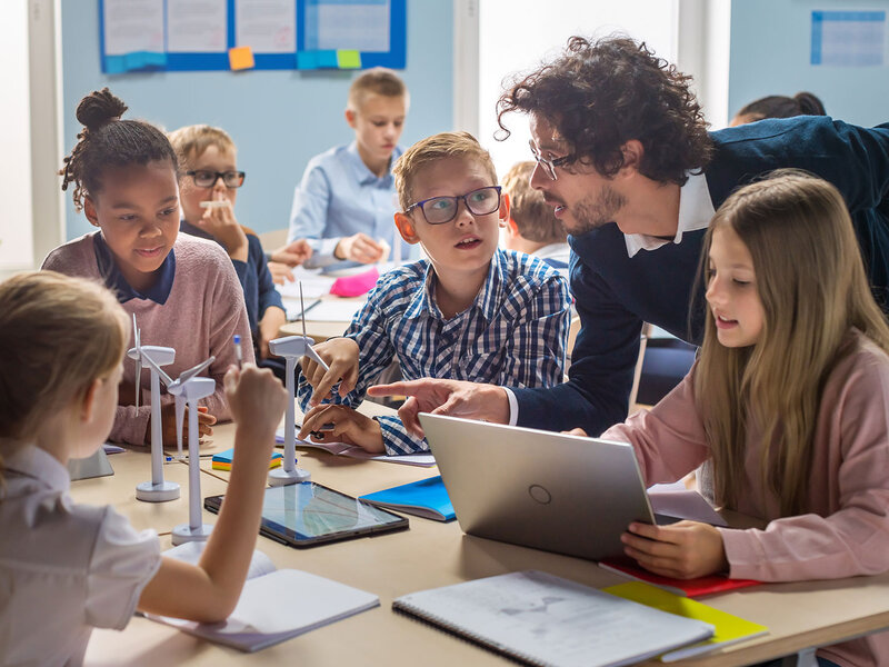 In einer Grundschule lernen Kinder gemeinsam mit ihrem Lehrer an Tablets und Modellen von Windrädern.