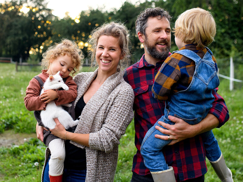 Ein Vater und eine Mutter stehen auf einer Wiese und halten ihre Kinder auf den Armen