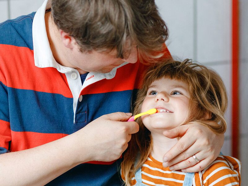 Ein Vater putzt seiner kleinen Tochter die Zähne.