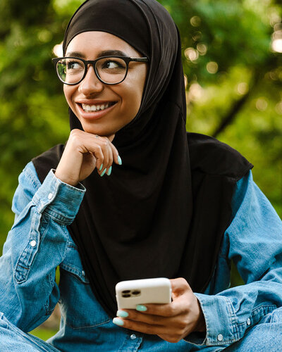 Mädchen im Schneidersitz lächelt, hält Mobiltelefon in der Hand
